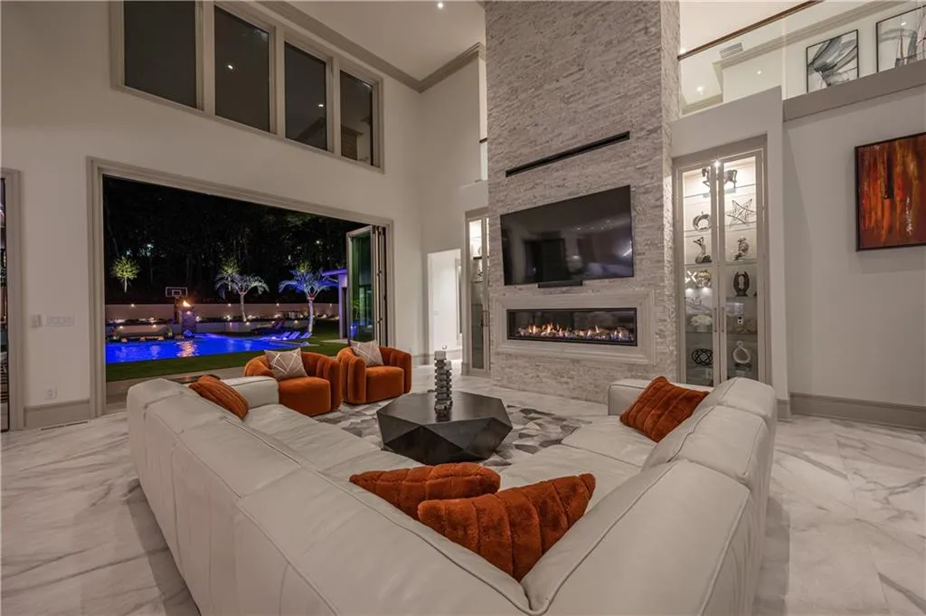 Two-story living area featuring a stacked stone accent wall with an integrated linear fireplace, built-in display cabinetry, and enchanting evening pool views