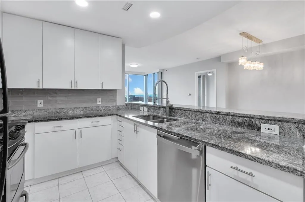 Kitchen featuring stainless steel appliances, dark stone counters, white cabinets, light tile patterned floors, and pendant lighting