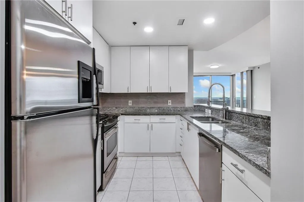 Kitchen featuring appliances with stainless steel finishes, dark stone counters, tasteful backsplash, white cabinets, and light tile patterned flooring