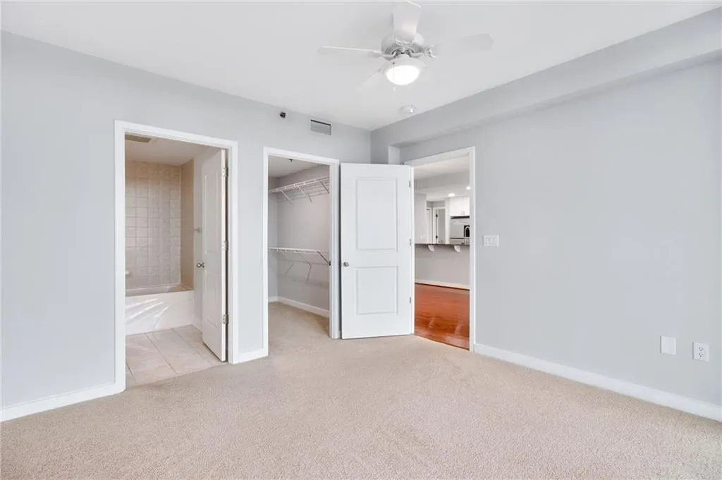 Unfurnished bedroom featuring light colored carpet, a spacious closet, connected bathroom, and ceiling fan