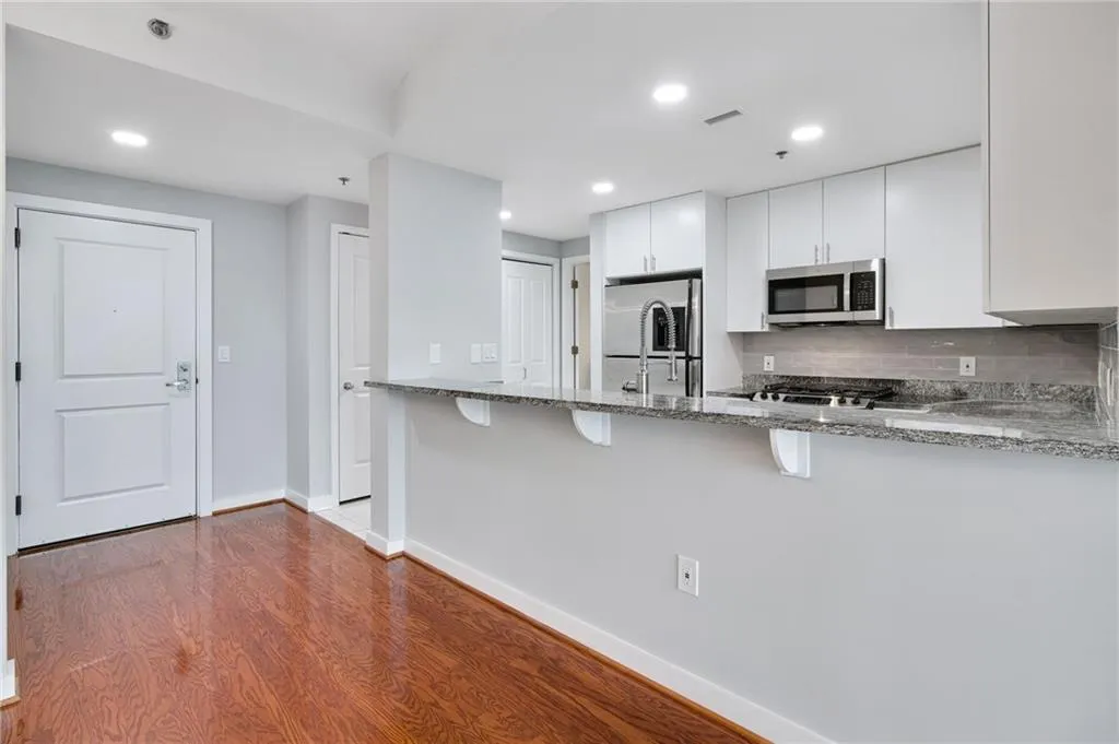 Kitchen with light stone countertops, a peninsula, a kitchen breakfast bar, stainless steel microwave, and white cabinets