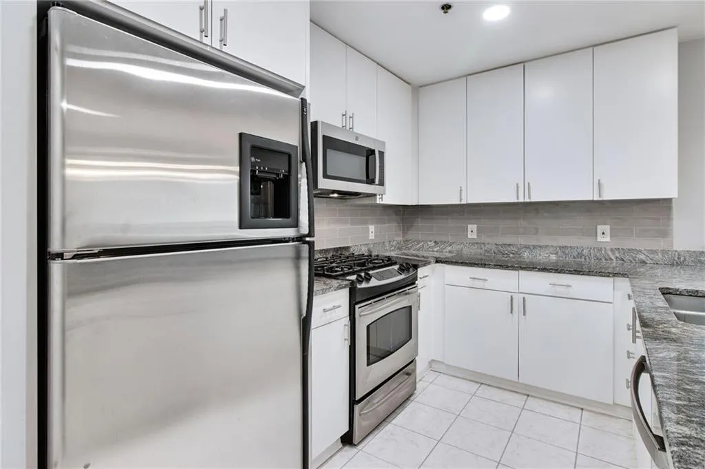 Kitchen with stainless steel appliances, decorative backsplash, white cabinetry, and dark stone countertops