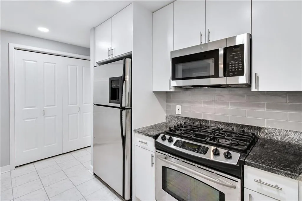 Kitchen featuring appliances with stainless steel finishes, white cabinets, tasteful backsplash, dark stone countertops, and recessed lighting