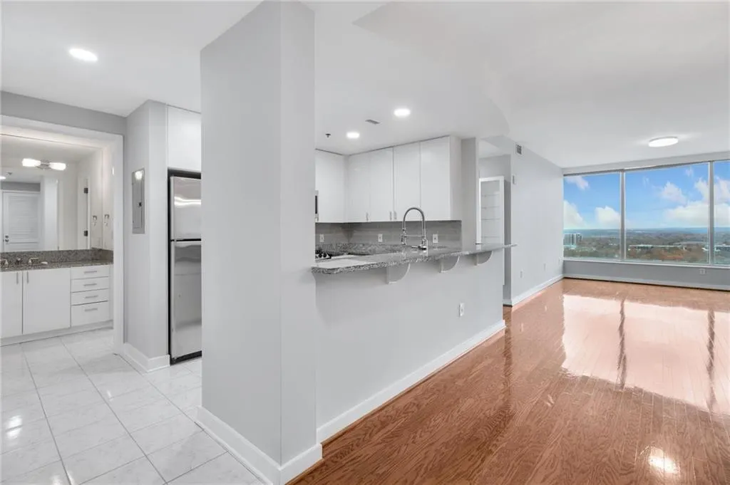 Kitchen featuring light stone counters, white cabinetry, a kitchen breakfast bar, backsplash, and freestanding refrigerator
