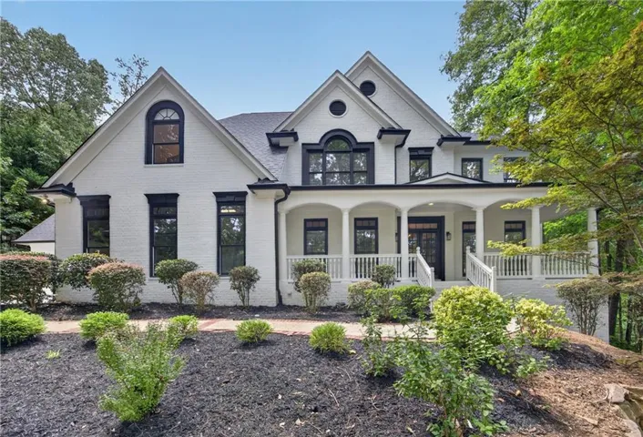 White brick exterior with black trim, covered porch, arched windows, and manicured landscaping