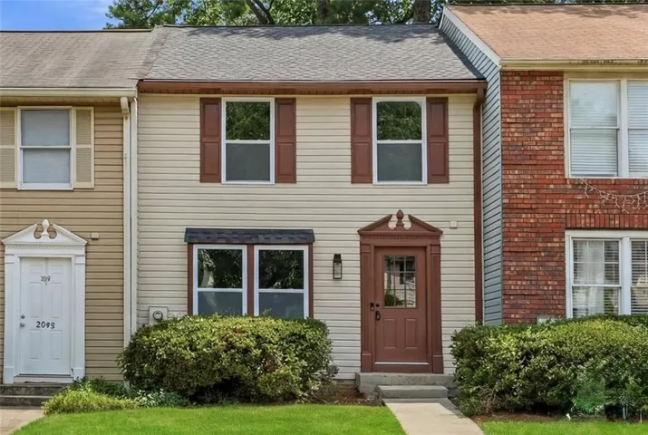 Two-story townhouse with light-colored siding and a brown-trimmed front door featuring decorative millwork