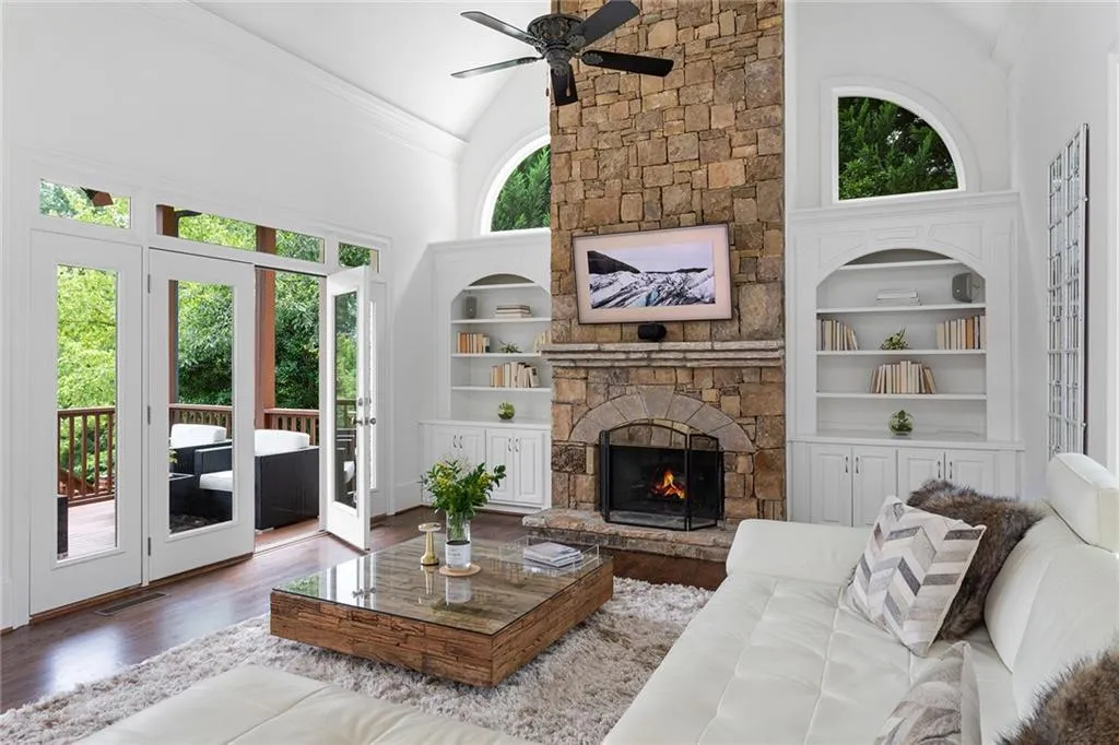 Living room with built in shelves, plenty of natural light, a stone fireplace, and ceiling fan