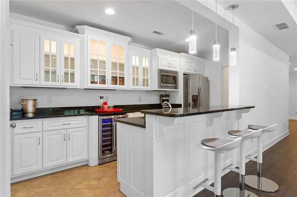 Kitchen with a breakfast bar, stainless steel appliances, beverage cooler, decorative light fixtures, and white cabinetry