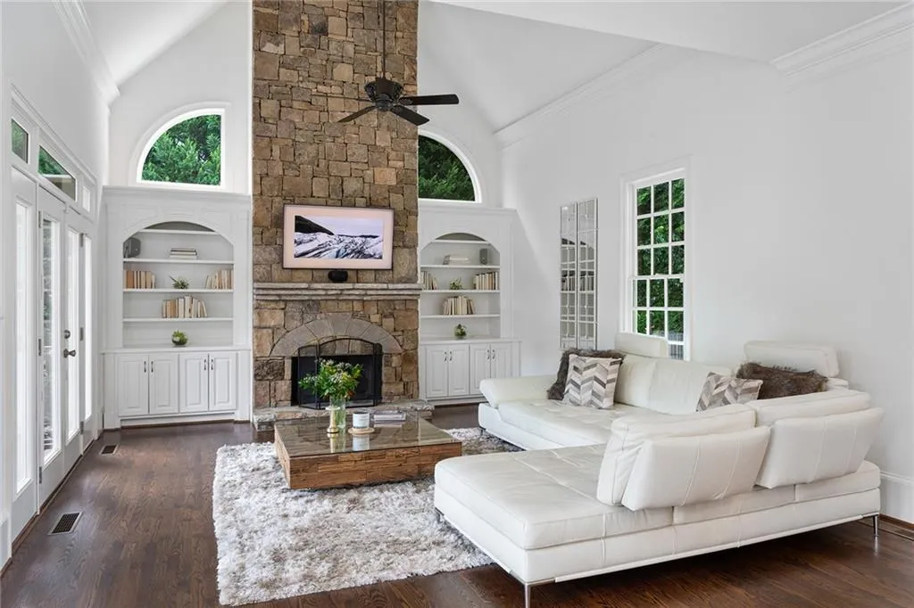 Living room with high vaulted ceiling, dark wood-type flooring, a fireplace, built in features, and ceiling fan