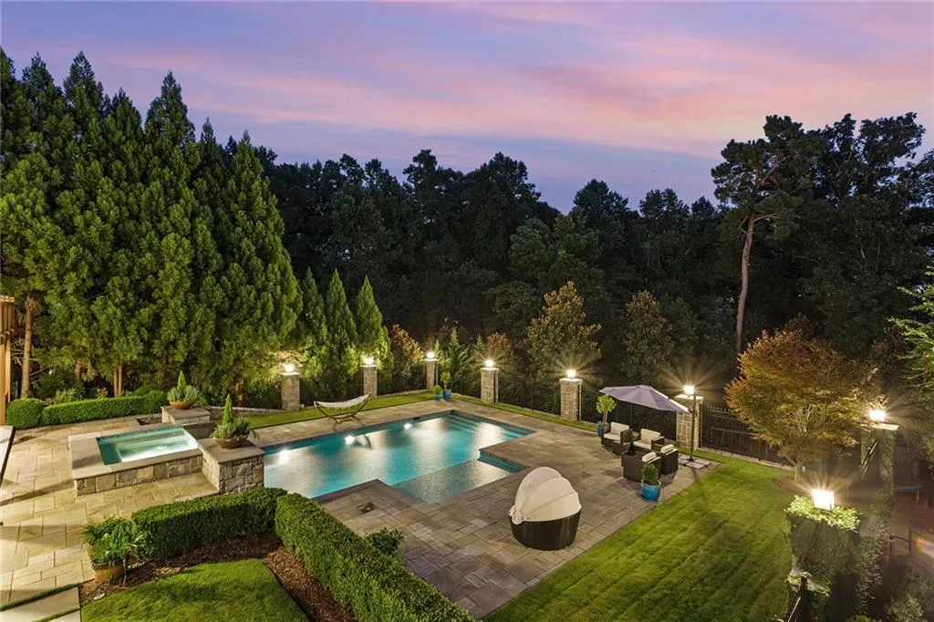 Pool at dusk featuring a patio, a lawn, an in ground hot tub, and pool water feature