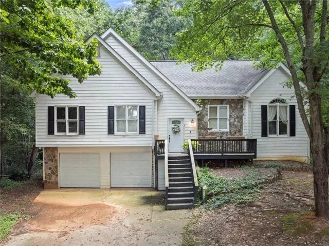 White siding exterior with a stone accent facade, dual garage doors, front porch, and a wood-finish deck