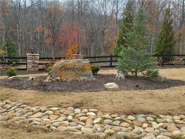 Stone-clad entry columns with integrated lighting, large natural stone signage, diverse evergreen plantings, and a decorative rock-lined channel