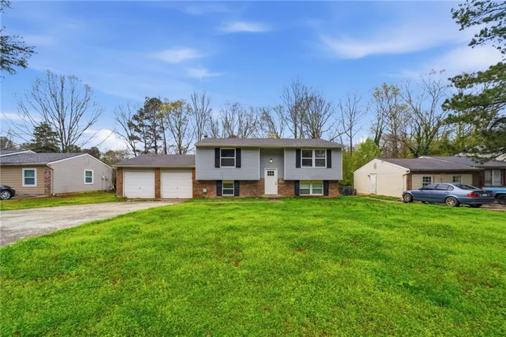 Bi-level home with brick siding, a garage, a front lawn, and driveway