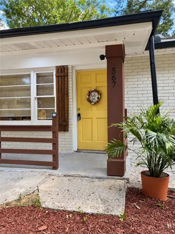White brick exterior with a vibrant yellow paneled door, dark brown exterior shutters, and a covered entryway