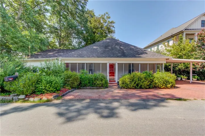Exterior featuring a screened porch, red entry door, attached carport, and mature landscaping
