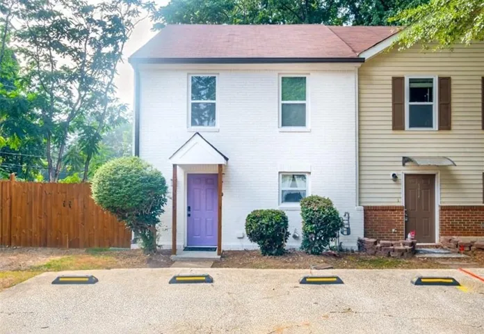 White brick exterior featuring a distinct purple entry door with an overhead portico