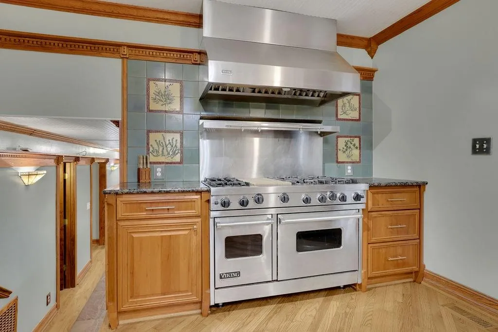 Kitchen featuring decorative backsplash, wall chimney exhaust hood, dark stone counters, ornamental molding, and premium stove