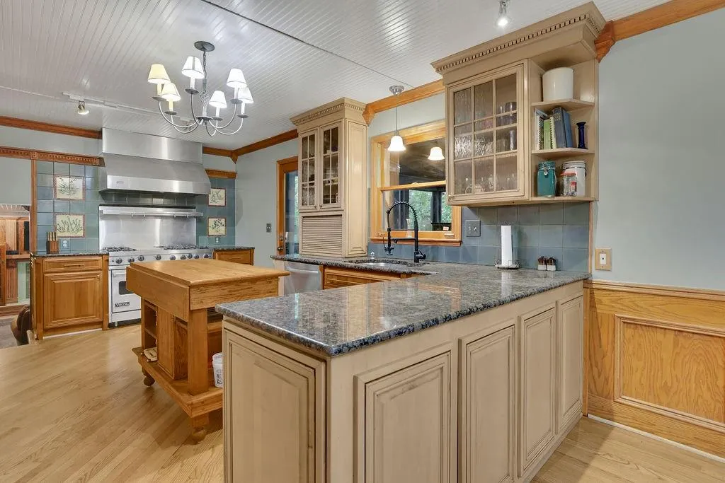 Kitchen with decorative backsplash, decorative light fixtures, dark stone counters, sink, and wall chimney range hood