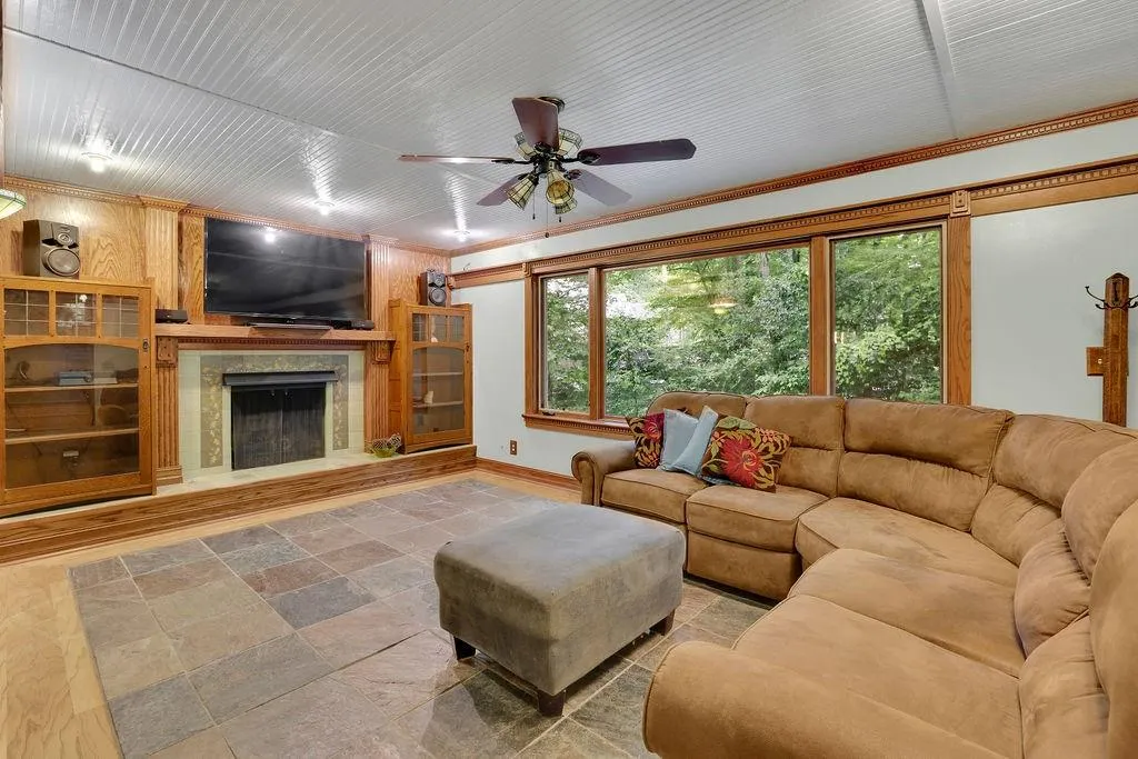 Living room featuring ceiling fan, wood walls, ornamental molding, a tile fireplace, and hardwood / wood-style floors