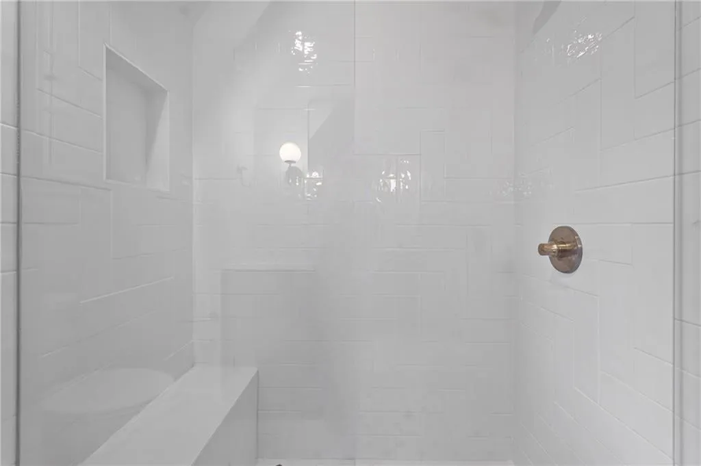 Enclosed shower with white tiled walls, a built-in bench, a recessed niche, and a bronze-finish shower control