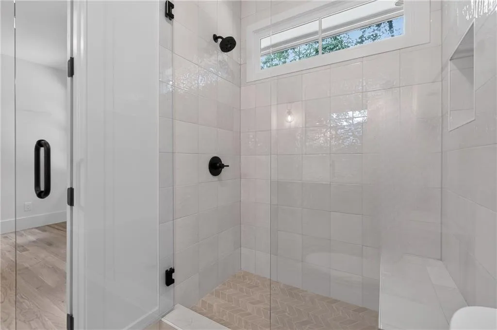 Glass-enclosed shower with matte black fixtures, integrated shower bench, tiled shower niche, and clerestory window