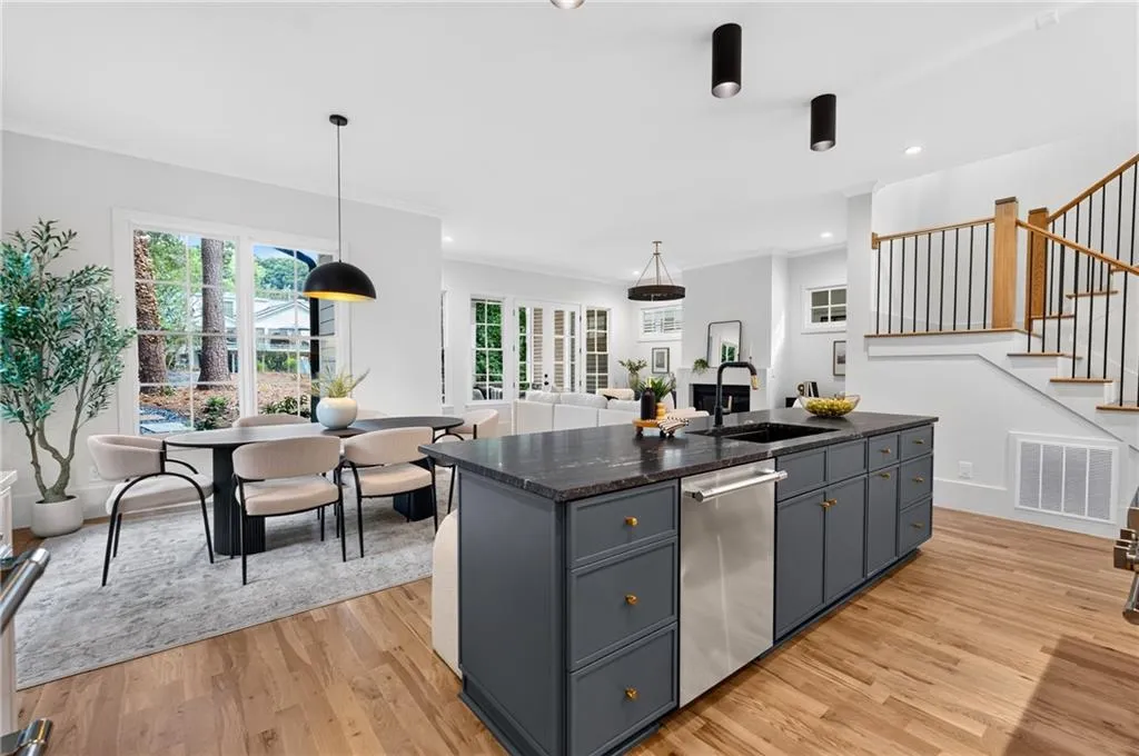 Open-concept kitchen and dining area featuring hardwood flooring, a dark-toned kitchen island with sink, and a staircase with wood and iron railings