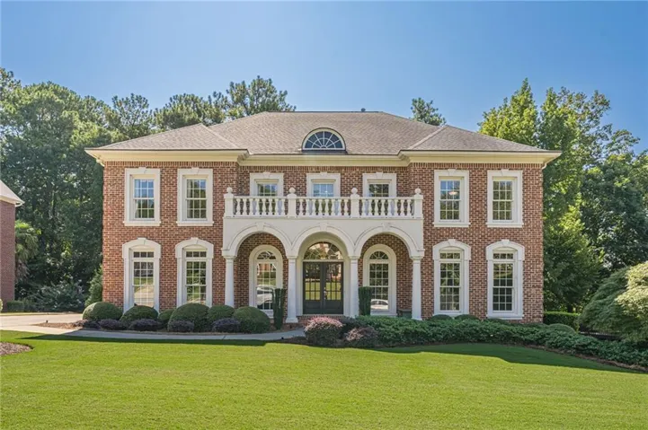Brick exterior with arched entry, second-story balcony, white window trim, and manicured landscaping