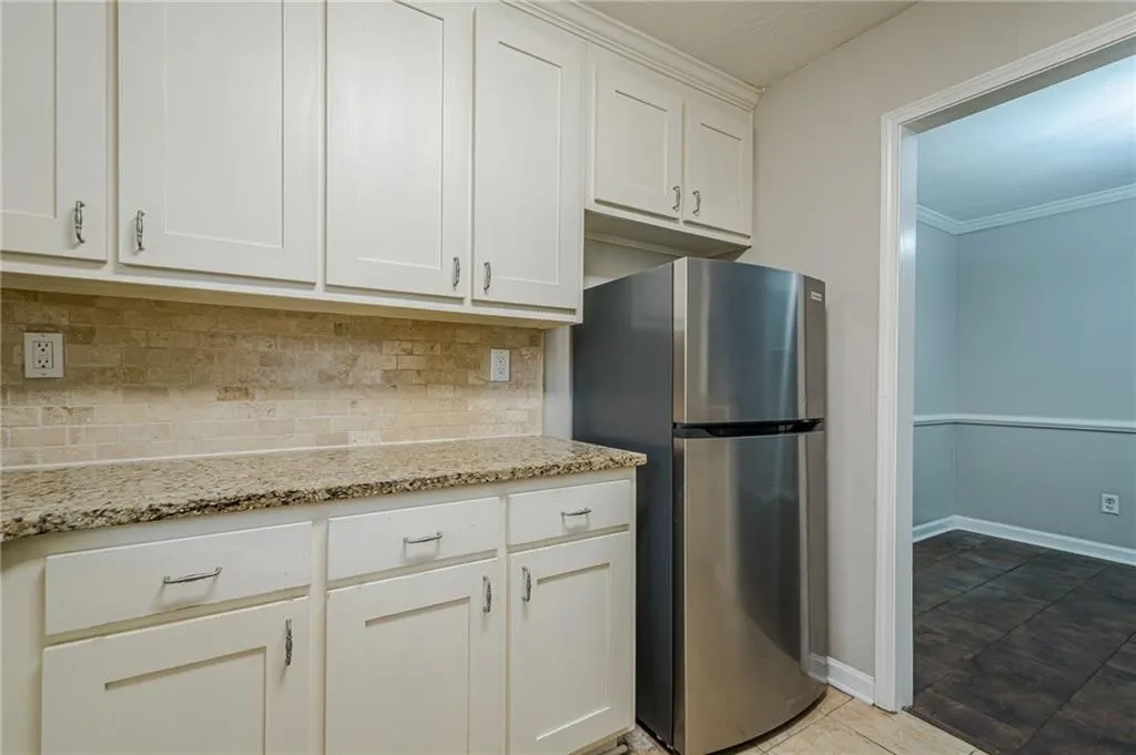 Kitchen with light stone countertops, ornamental molding, white cabinetry, freestanding refrigerator, and tasteful backsplash