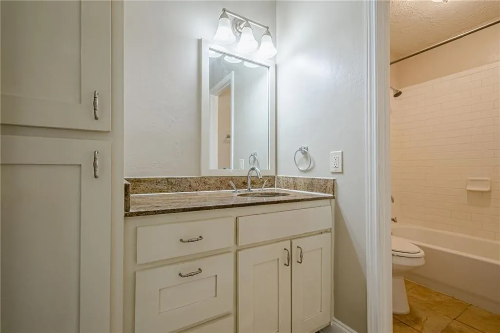 Bathroom with vanity, washtub / shower combination, a textured wall, and light tile patterned flooring