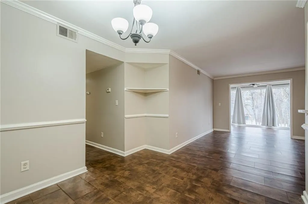 Unfurnished room with crown molding, a chandelier, and dark wood-style flooring