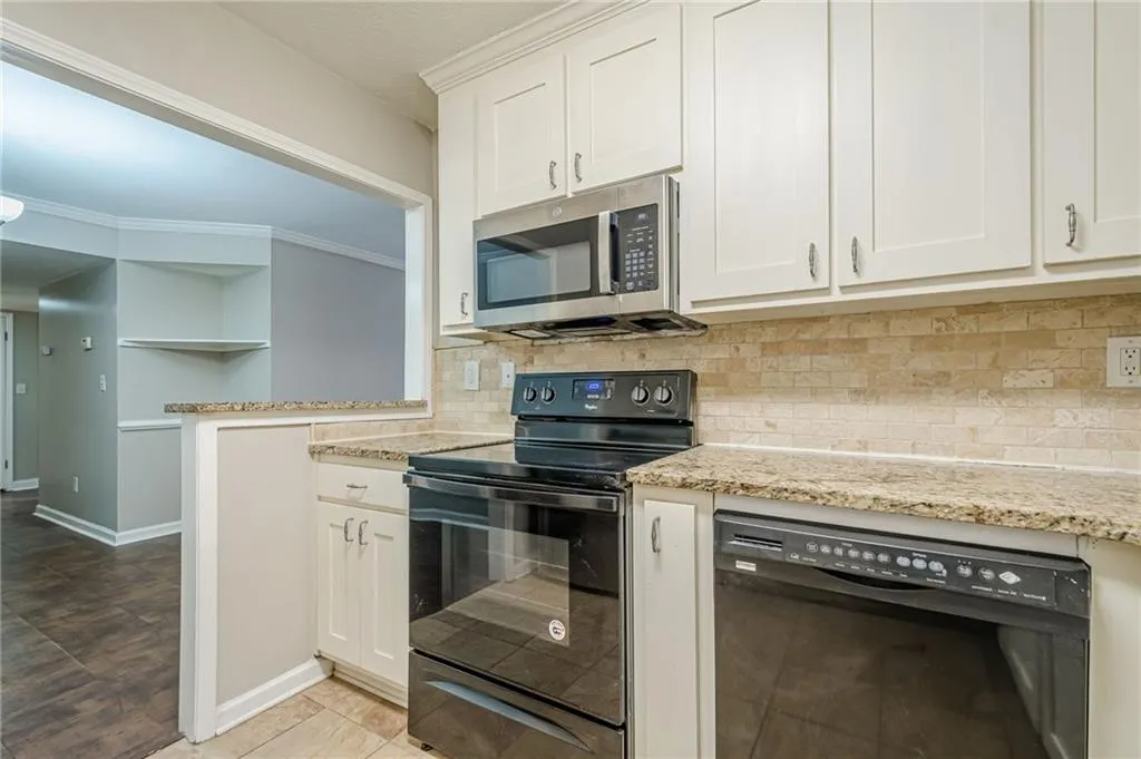 Kitchen with black appliances, white cabinetry, light stone countertops, tasteful backsplash, and ornamental molding