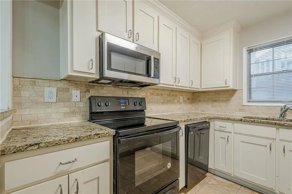 Kitchen featuring black appliances, white cabinets, light stone countertops, and light tile patterned flooring