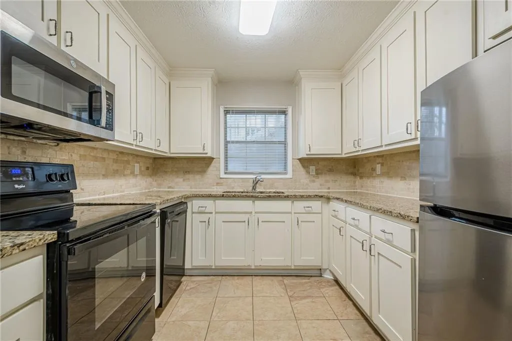 Kitchen with black appliances, white cabinets, light stone counters, and a textured ceiling