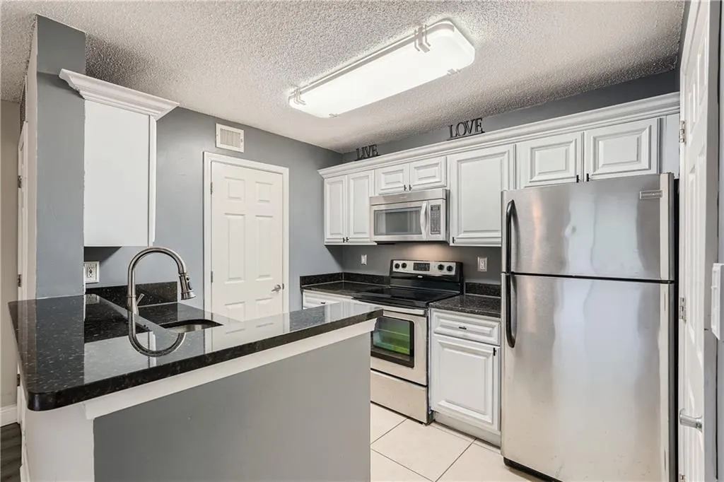Kitchen featuring dark stone countertops, a textured ceiling, stainless steel appliances, sink, and white cabinets