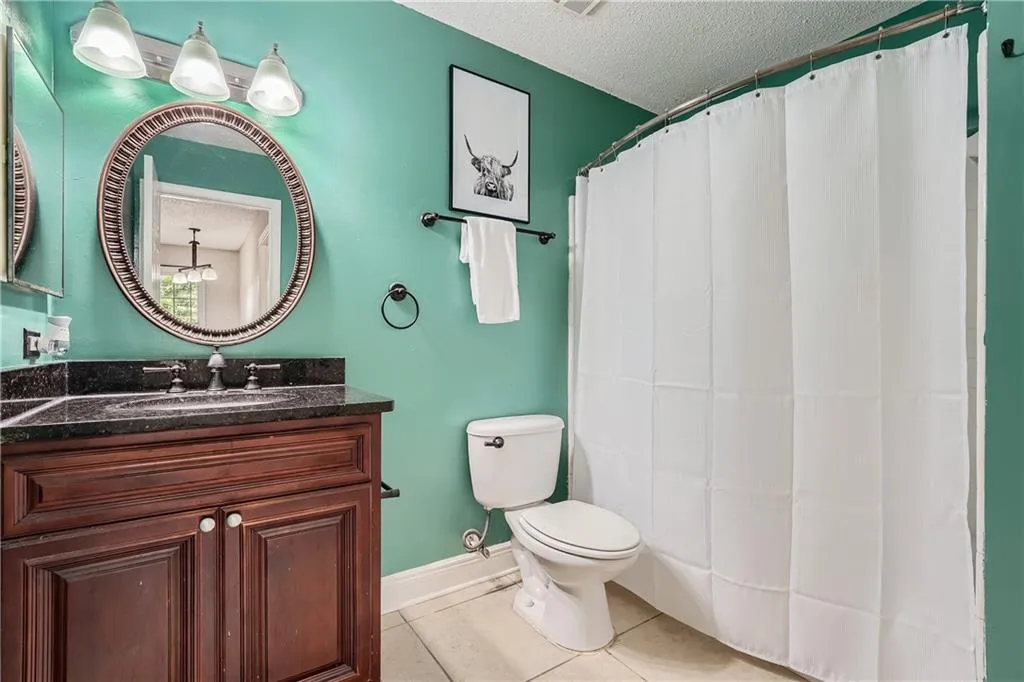 Bathroom featuring curtained shower, tile patterned floors, toilet, vanity, and a textured ceiling