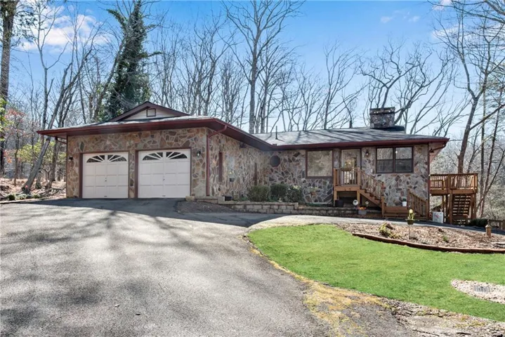 Stone veneer exterior with a two-car garage, an exterior wooden staircase, and a wooden deck