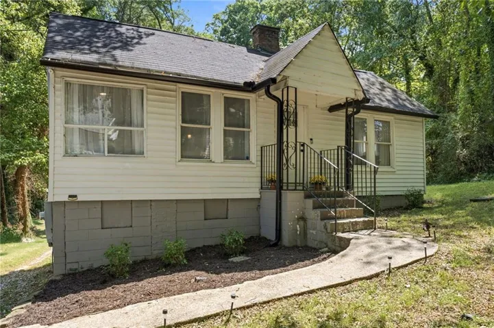 White siding exterior with a dark shingle roof, featuring a covered entry, black iron handrails, and a concrete walkway