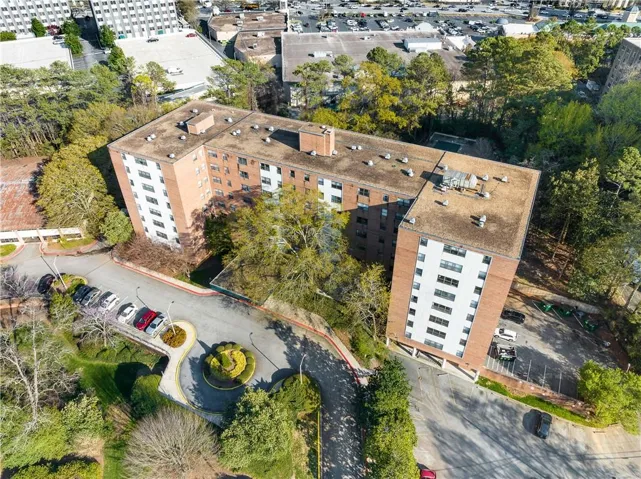 Brick-clad multi-story building featuring multiple wings, a surface parking area, and mature landscaping