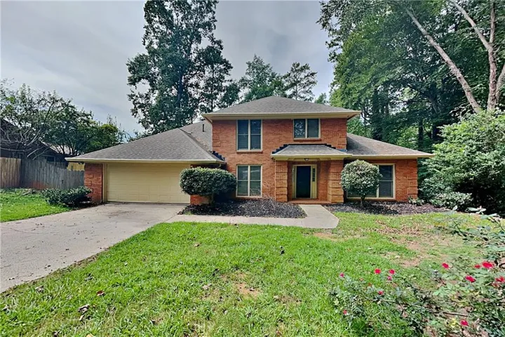 Brick exterior, attached two-car garage, concrete driveway, mature landscaping, and an inviting front walkway