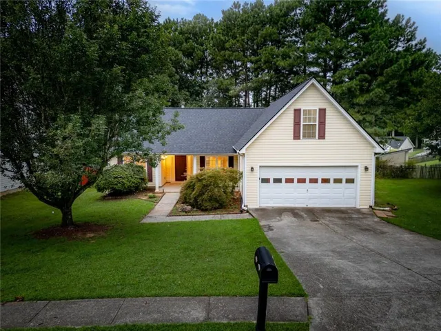 Single-story residence featuring light-toned siding, a dark shingle roof, and a prominent front-facing garage with a decorative paneled door