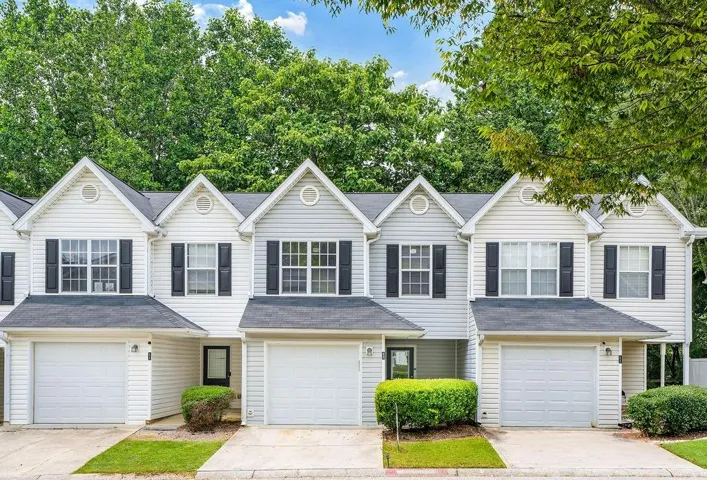 White siding townhome exterior featuring individual garage access and black window shutters