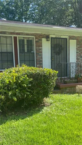 Brick exterior featuring a security screen door, white window shutters, and a manicured hedge