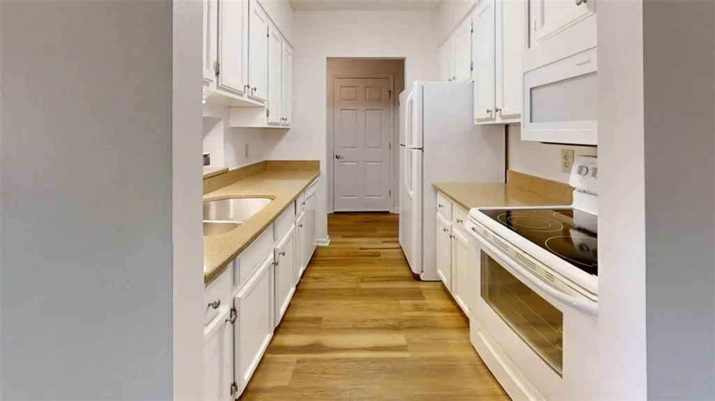 Kitchen featuring white appliances, white cabinetry, light wood-style flooring, and light stone counters