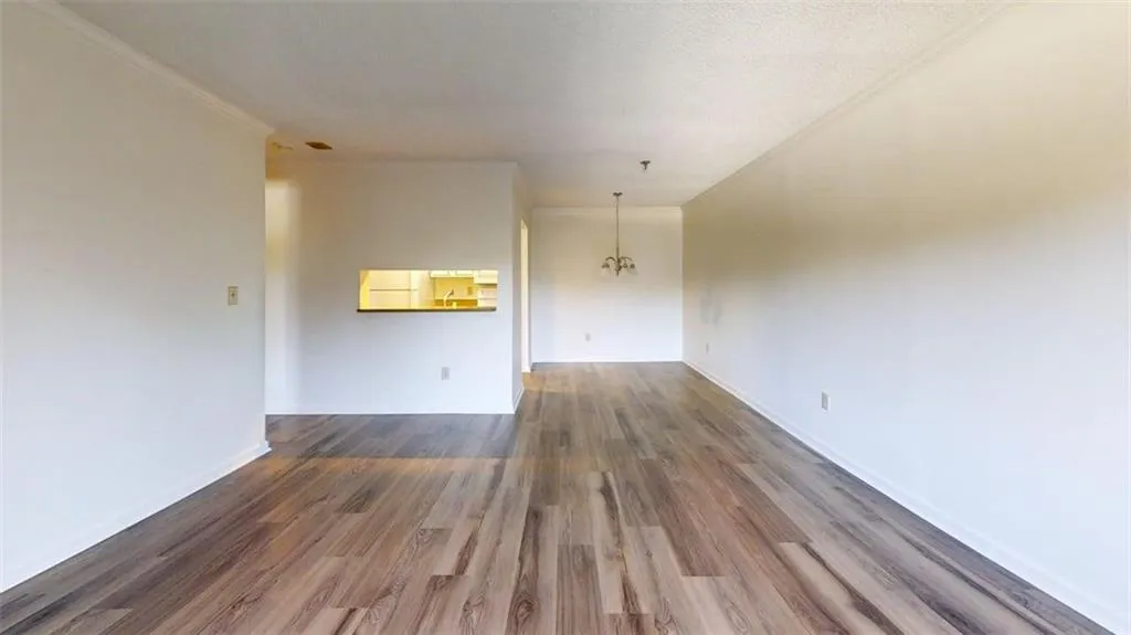 Unfurnished living room with dark wood-type flooring, a chandelier, and ornamental molding