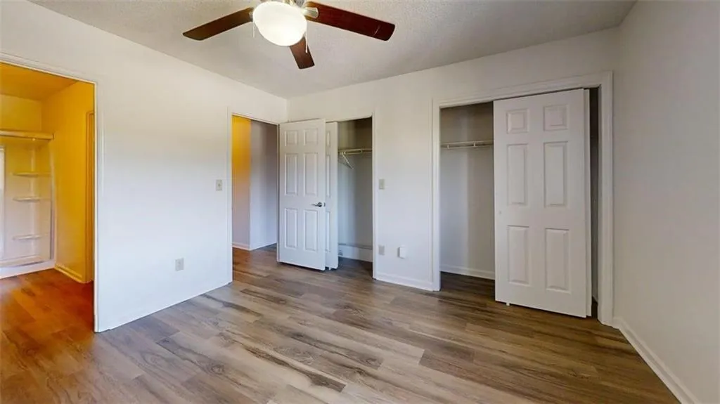 Unfurnished bedroom featuring two closets, wood finished floors, ceiling fan, and a textured ceiling