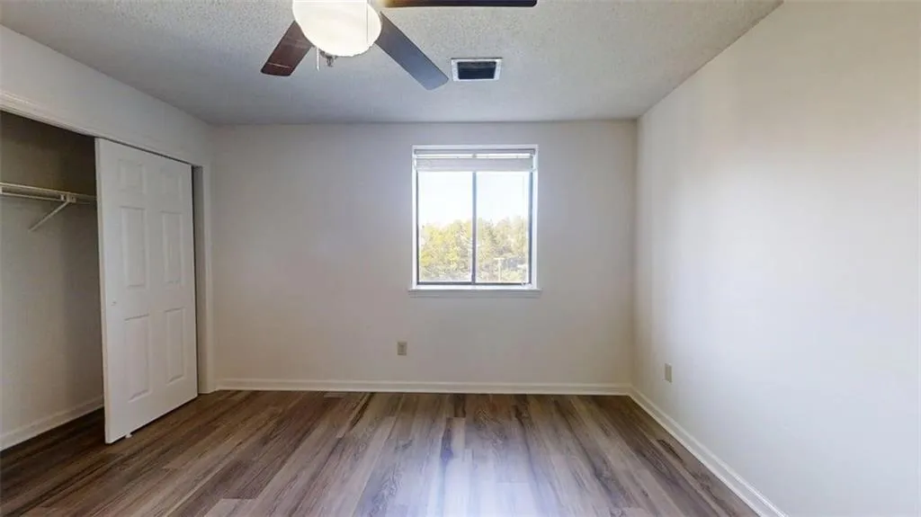 Unfurnished bedroom with dark wood-style floors, a textured ceiling, a closet, and ceiling fan
