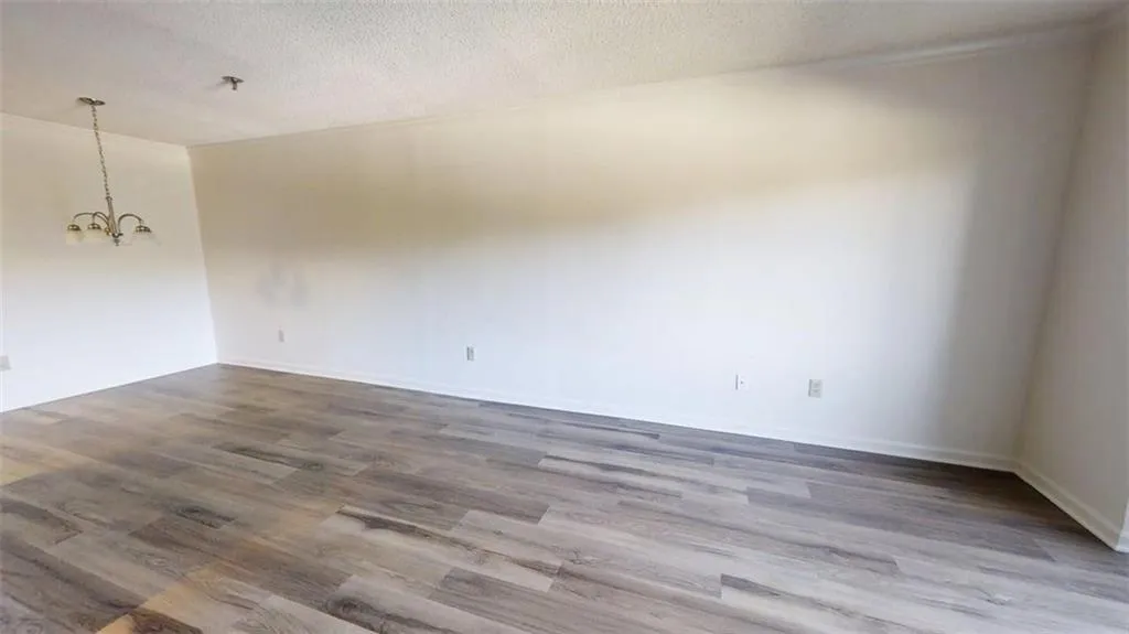 Empty room featuring a textured ceiling, wood finished floors, and a chandelier