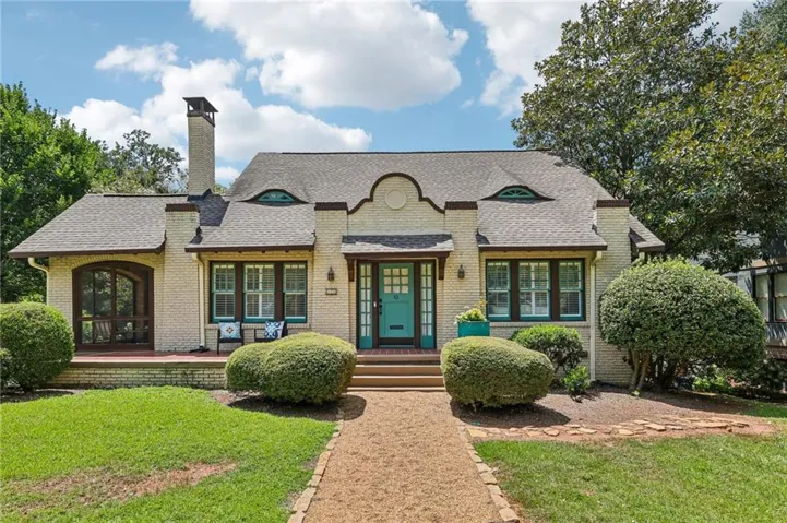 Brick exterior featuring a teal front door, decorative dormer windows, a prominent chimney, and a gravel walkway