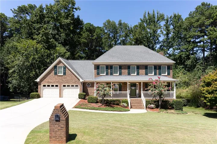 Traditional brick two-story residence featuring a covered front porch, white railings, a multi-pane front door, and a two-car garage