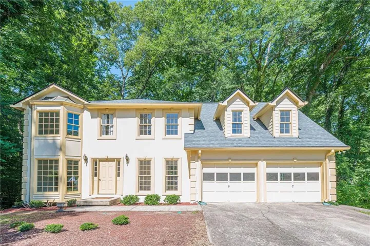 Light-colored two-story residence featuring a prominent bay window structure, dual dormers, and a two-car garage